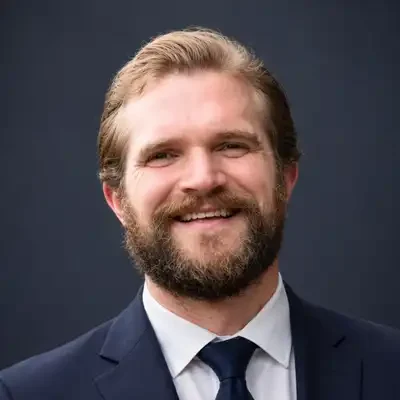 Chiropractor Exeter NH Person in a navy suit and tie with a beard, smiling in a professional headshot.